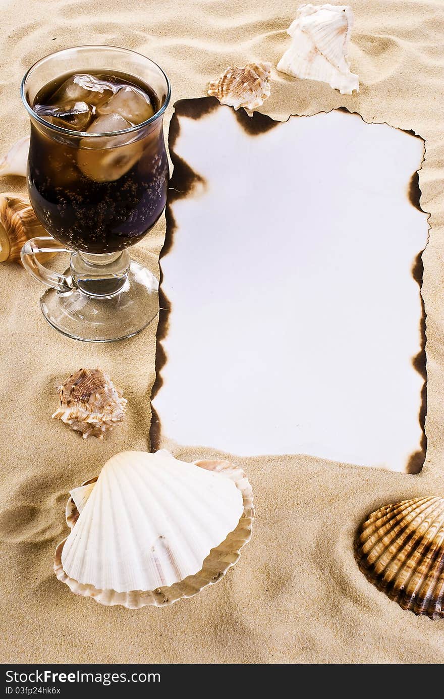 Burned paper on the sand with shells and ice cold drink. Burned paper on the sand with shells and ice cold drink