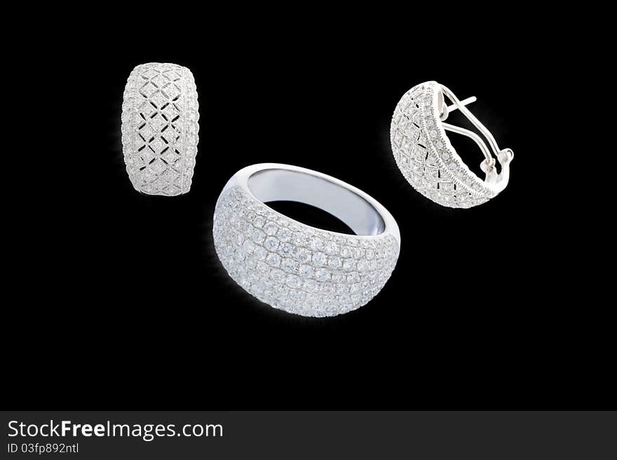 Set of two earrings and ring from white gold with plenty of brilliants on isolated black background. Set of two earrings and ring from white gold with plenty of brilliants on isolated black background