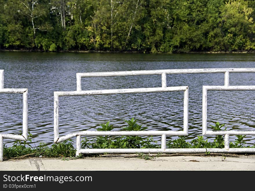 An old crooked white and rusted fence by a river bank. An old crooked white and rusted fence by a river bank.