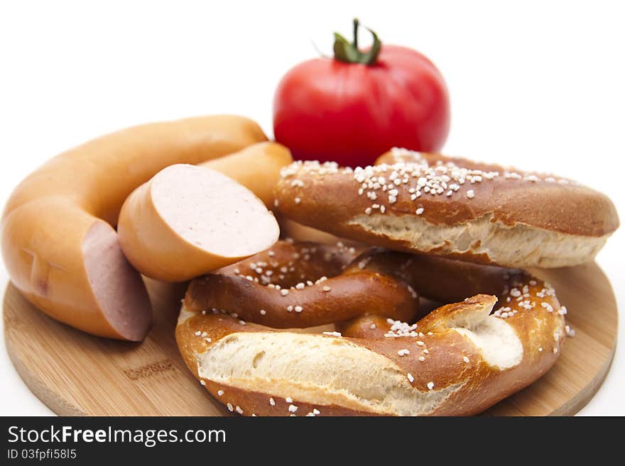 Meat sausage with salt pretzel and tomato onto wood plates