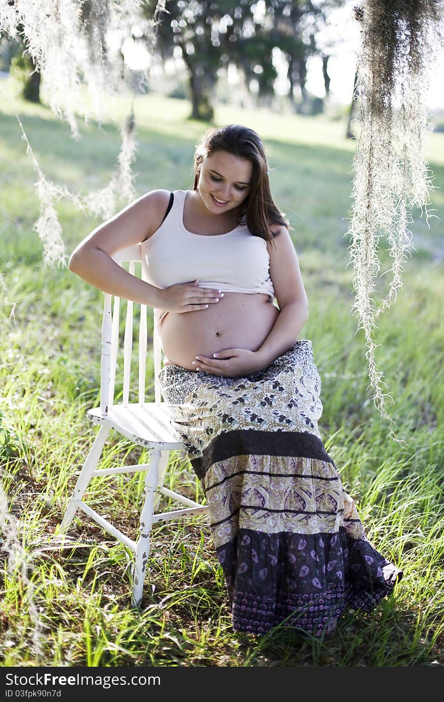 Pregnant woman sitting outside touching and looking at her bare belly.