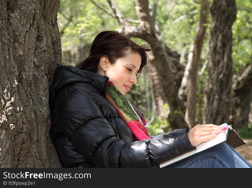 Side view of girl sitting and reading a book by a tree. Side view of girl sitting and reading a book by a tree