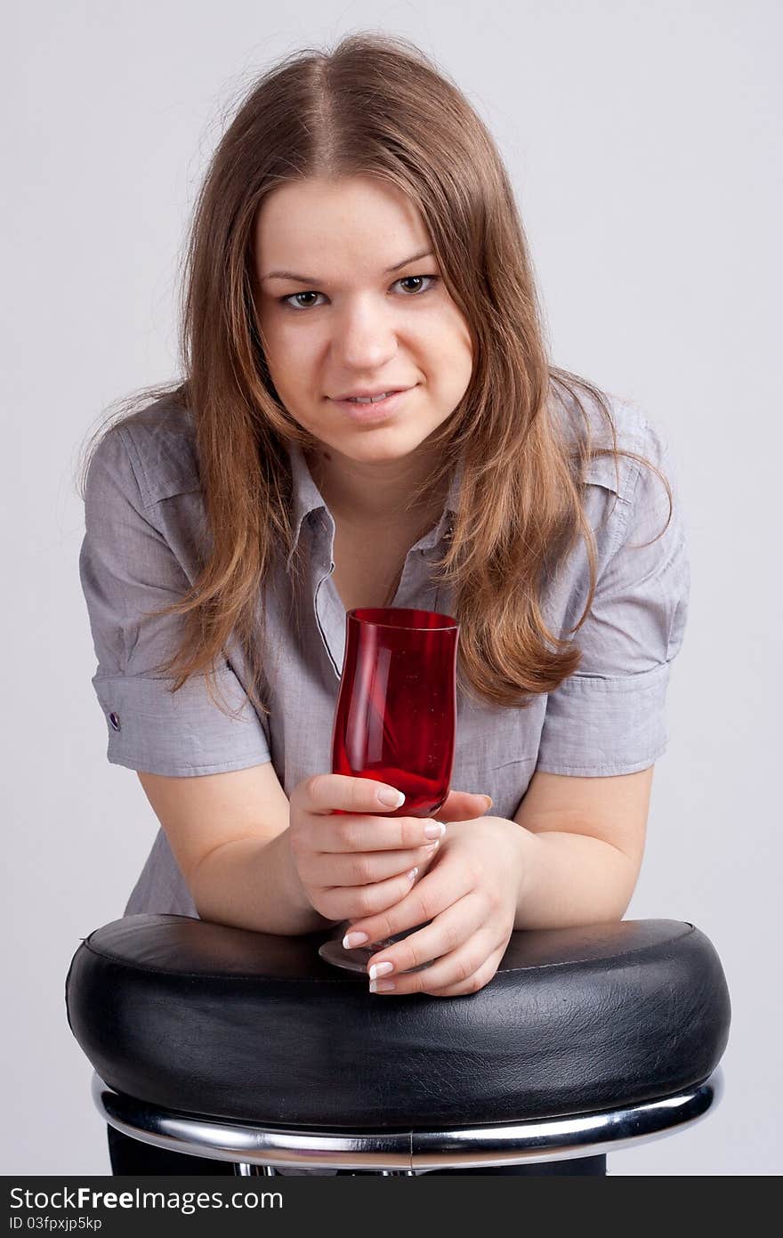 A girl in a bright red T-shirt and a glass sitting on a light background