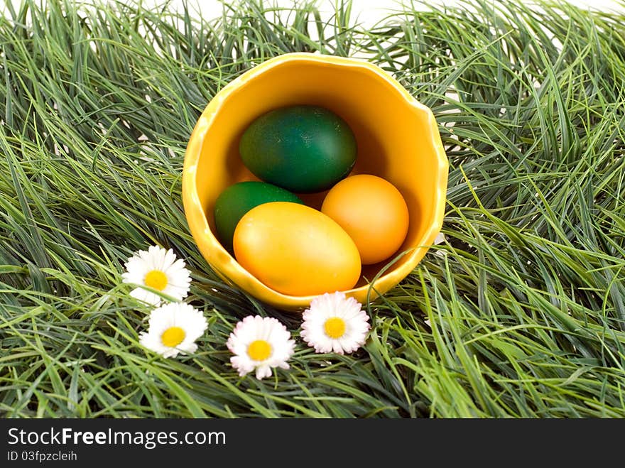 Yellow and green eggs in the big eggshell, placed with daisies on a green grass. Studio shot. Yellow and green eggs in the big eggshell, placed with daisies on a green grass. Studio shot.