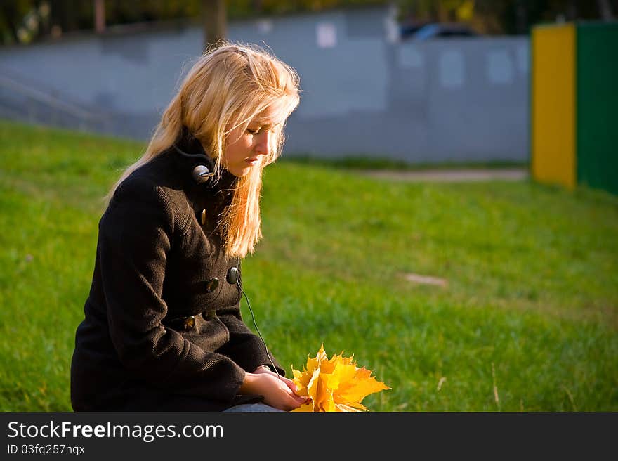 Teenage girl with long blond hair looking at a bouquet of yellow autumn leaves. Teenage girl with long blond hair looking at a bouquet of yellow autumn leaves