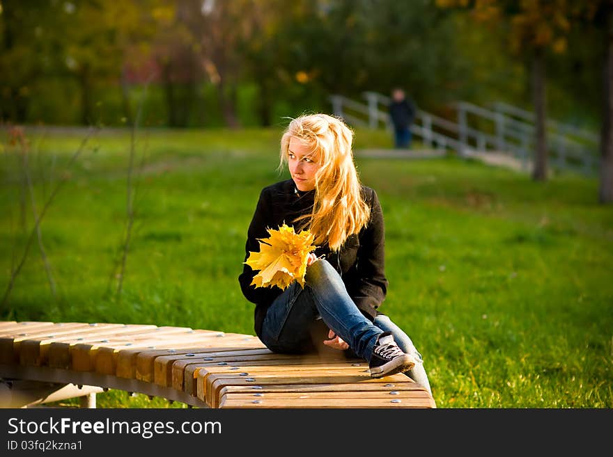 Teenage girl with long blond hair looking at a bouquet of yellow autumn leaves. Teenage girl with long blond hair looking at a bouquet of yellow autumn leaves