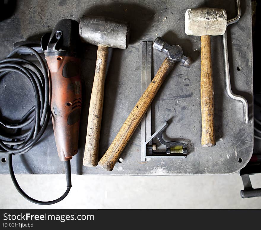 Mallets, hammers, grinder and ruler sitting on a steel table covered in sawdust. Mallets, hammers, grinder and ruler sitting on a steel table covered in sawdust