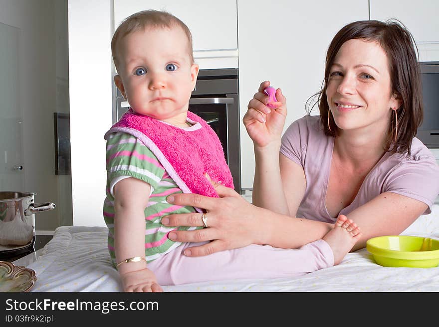 Young mother is feeding her baby in a modern kitchen setting. Young mother is feeding her baby in a modern kitchen setting.