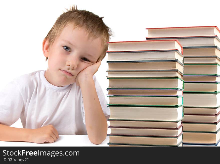 Tired schoolboy sits at the table with piles of books