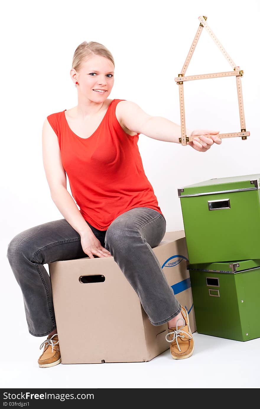 A young woman with a folding rule as a house symbol sits on moving box. A young woman with a folding rule as a house symbol sits on moving box