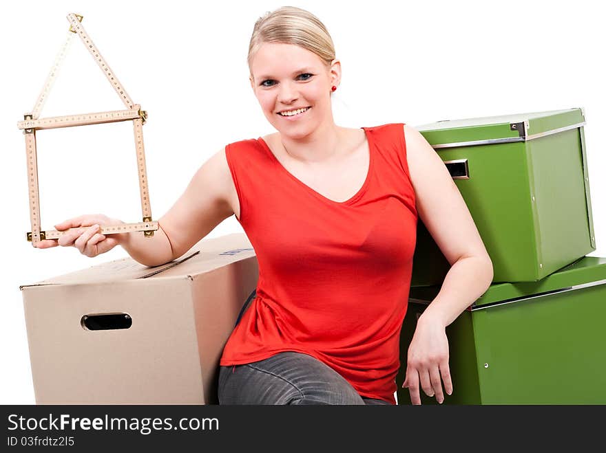 Young woman with a folding rule as a house symbol sits between move cardboards. Young woman with a folding rule as a house symbol sits between move cardboards