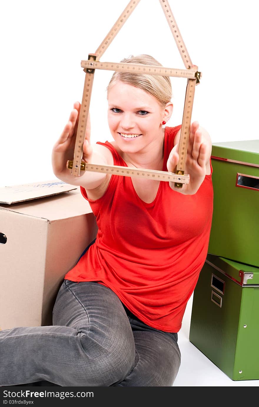 Young woman with a folding rule as a house symbol sits between move cardboards. Young woman with a folding rule as a house symbol sits between move cardboards