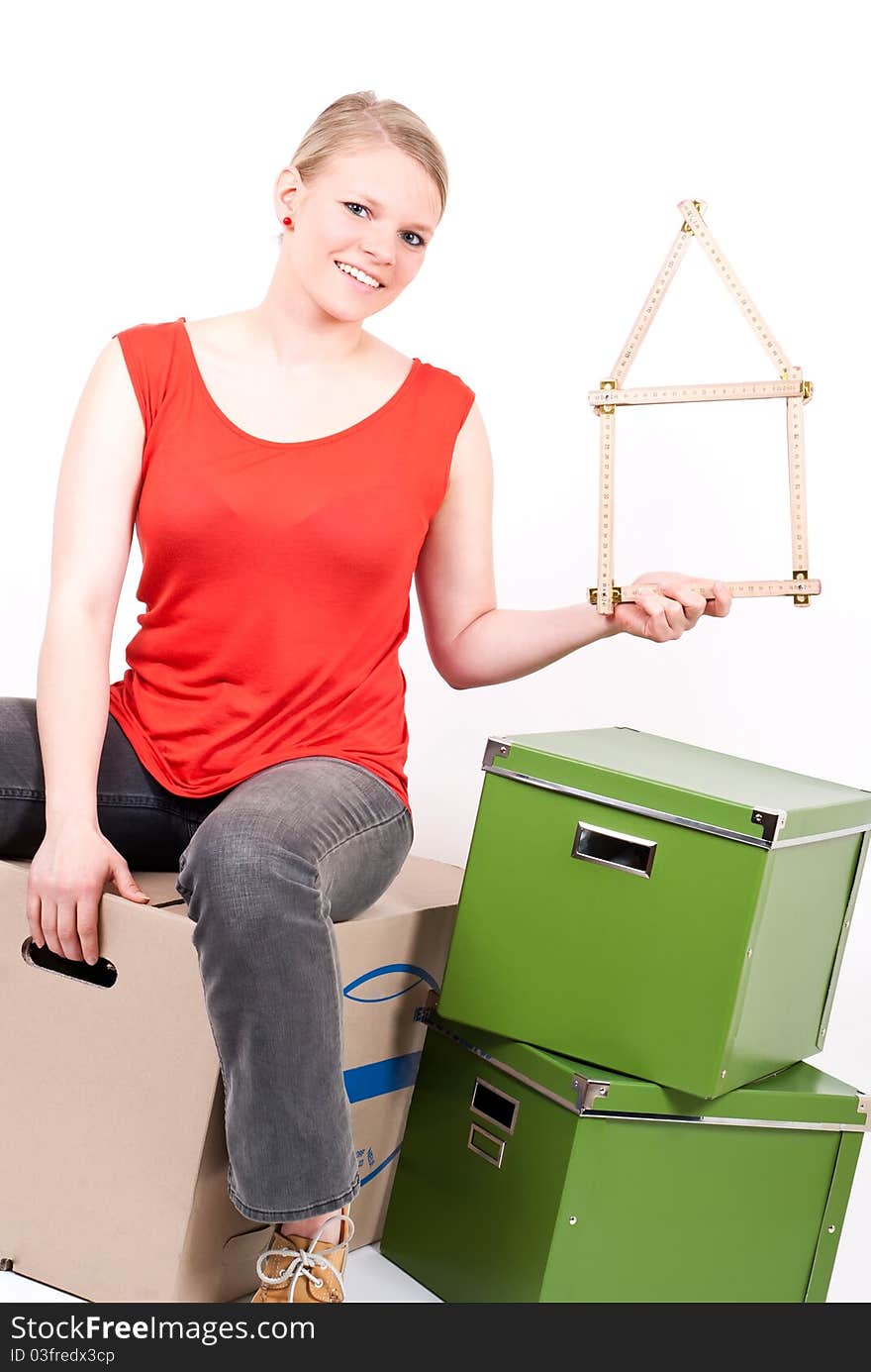 A young woman with a folding rule as a house symbol sits on moving box. A young woman with a folding rule as a house symbol sits on moving box