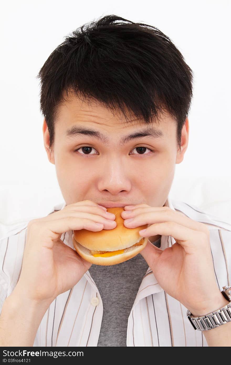 A hungry young Asian man biting into a burger against white background. A hungry young Asian man biting into a burger against white background