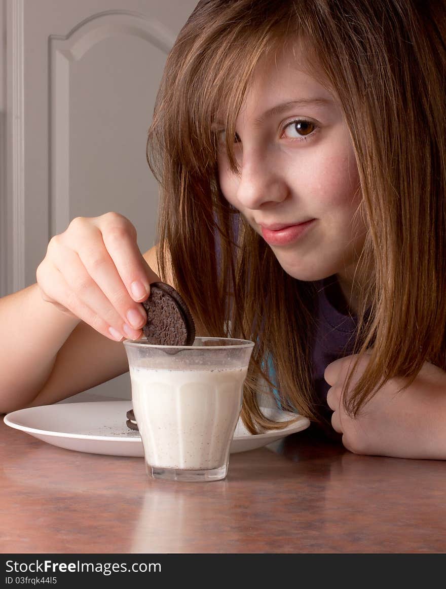 Cute girl looks while dunking a chocolate cookie in milk. Cute girl looks while dunking a chocolate cookie in milk