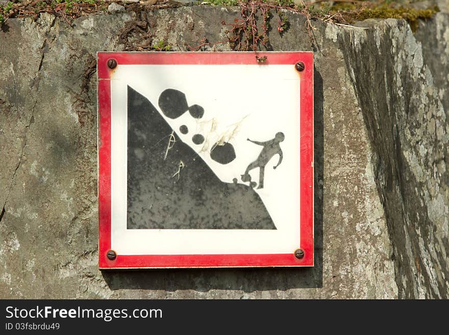 A square sign with red border showing the potential danger of falling rocks, fixed onto a wall with rusty screws. A square sign with red border showing the potential danger of falling rocks, fixed onto a wall with rusty screws.