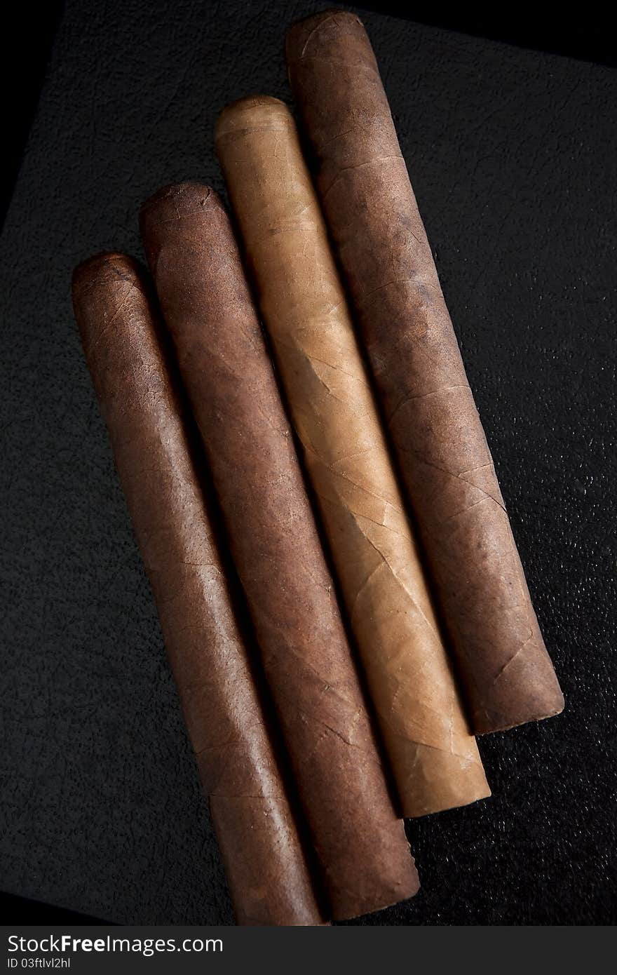 Four cigars on a dark background.