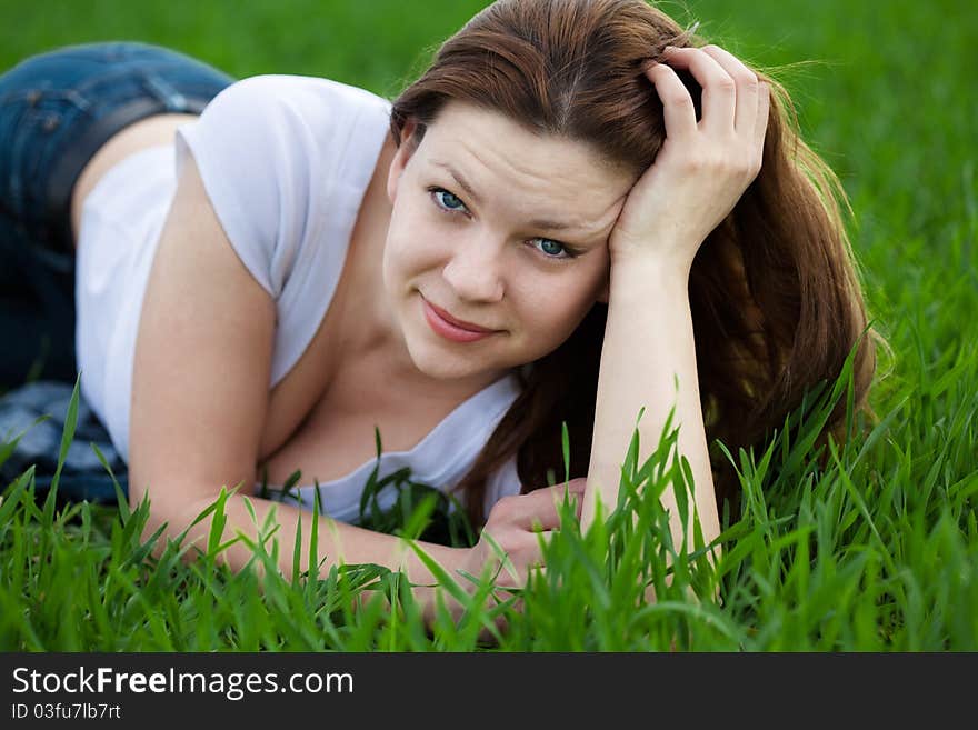 Cute woman dressed in white t-shirt and jeans lying in the grass in summer. Cute woman dressed in white t-shirt and jeans lying in the grass in summer