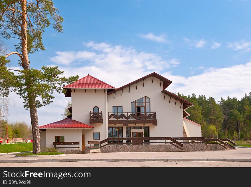 House with red roof against the backdrop of a pine forest