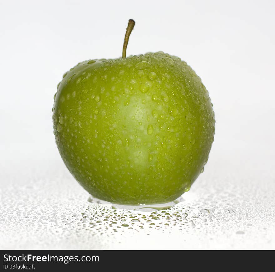 Green apple covered with water drops on a white background