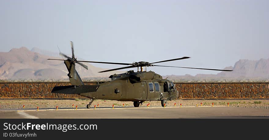 A military helicopter (Black Hawk) on helipad outdoor behind a stone wall, mountains and clear sky. A military helicopter (Black Hawk) on helipad outdoor behind a stone wall, mountains and clear sky