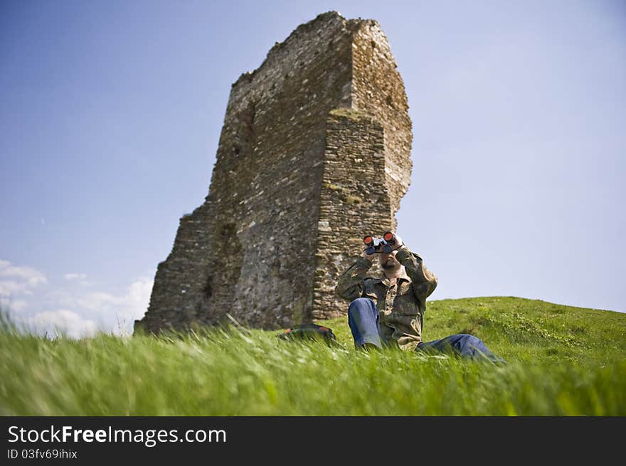 Man with binoculars looking out over hills and a tower fortress in the background