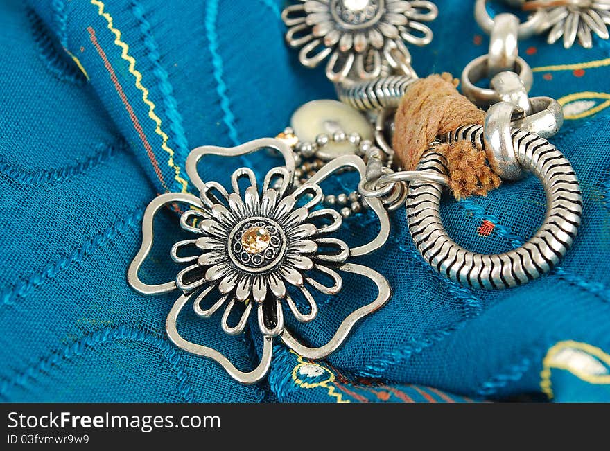 Silver necklace with flowers on the blue fabric  in East style background. Silver necklace with flowers on the blue fabric  in East style background.