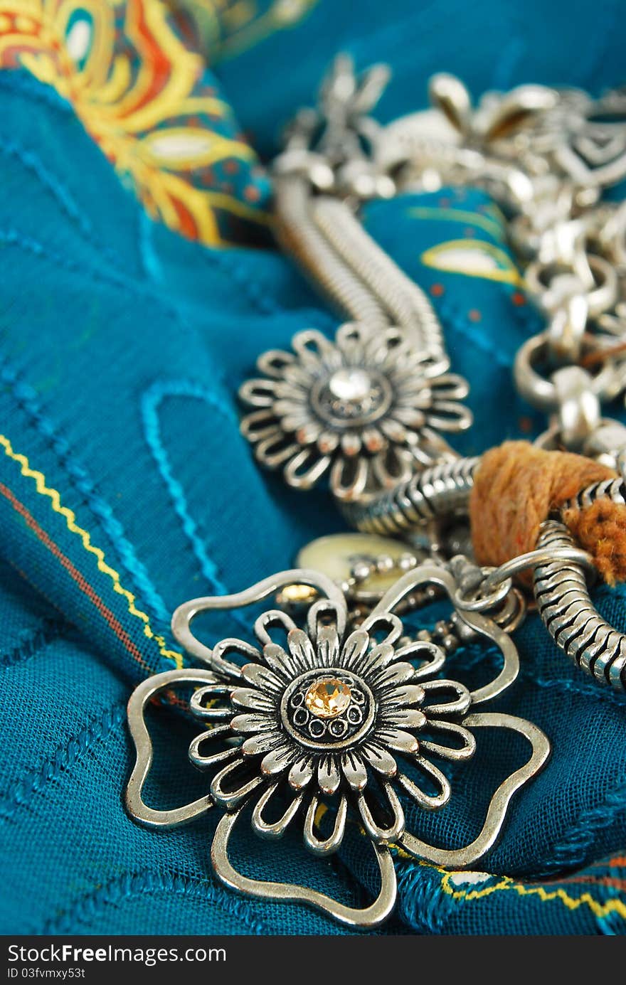 Silver necklace with flowers on the blue fabric in East style background. Silver necklace with flowers on the blue fabric in East style background.