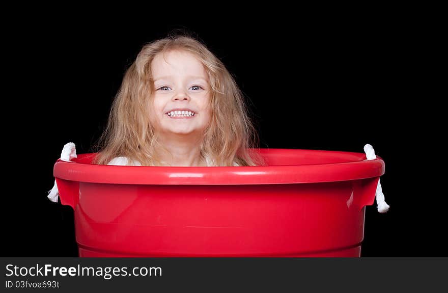 A cute girl is playing in a red bucket. A cute girl is playing in a red bucket.