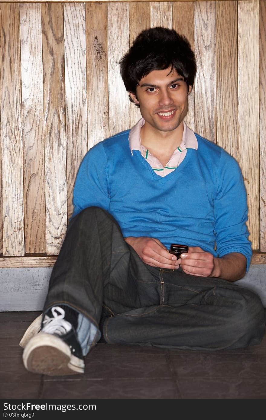 Young man sitting on floor with mobile phone smiling