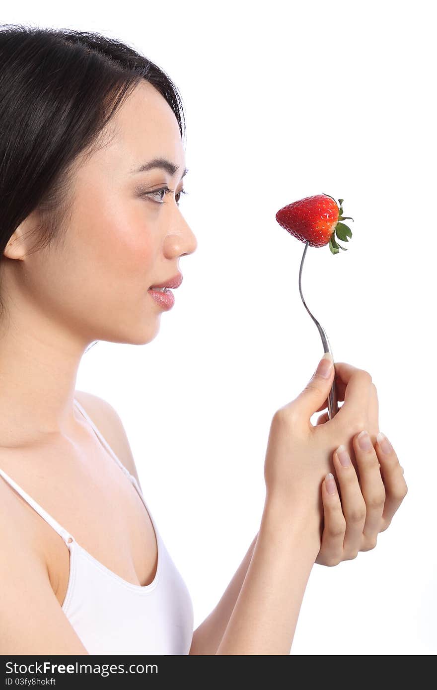 Beautiful smiling chinese teenager girl in profile, holding up a fresh red strawberry fruit on a fork. Beautiful smiling chinese teenager girl in profile, holding up a fresh red strawberry fruit on a fork.