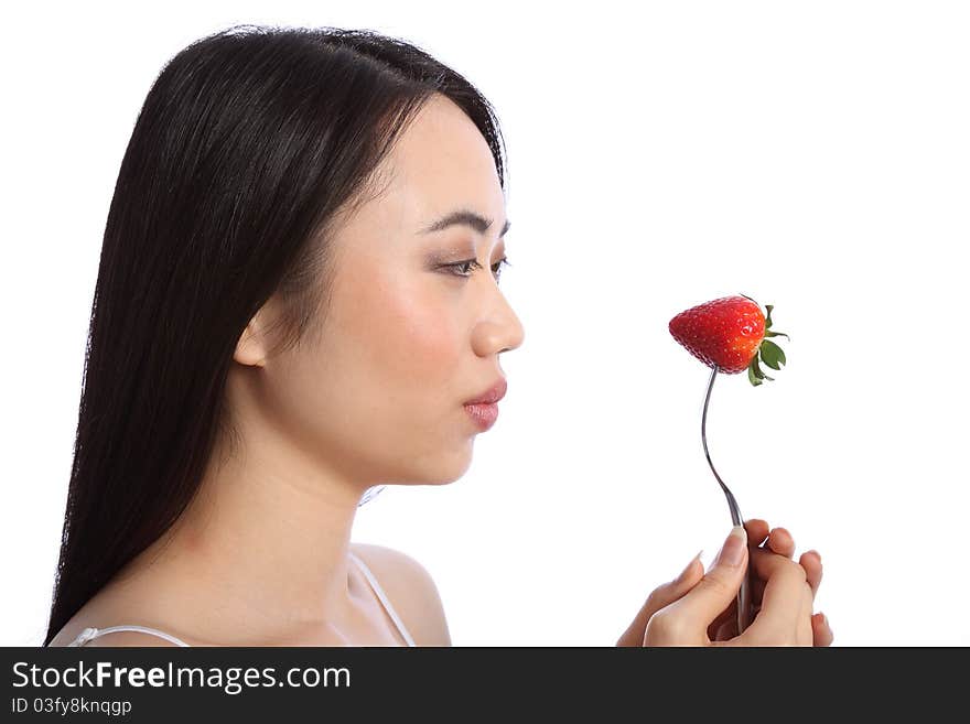 Beautiful young oriental teenager girl in profile, holding up a fresh red strawberry fruit on a fork. Beautiful young oriental teenager girl in profile, holding up a fresh red strawberry fruit on a fork.