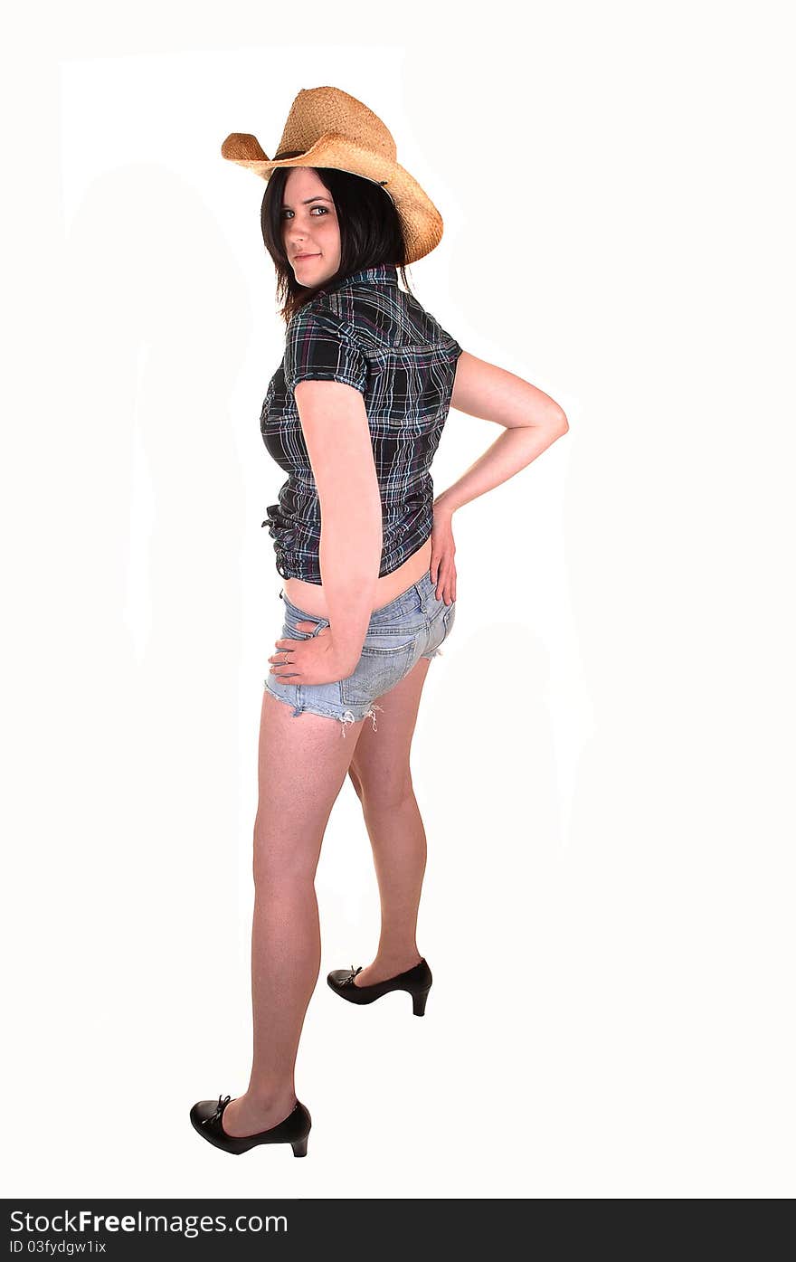 A lovely young woman in a blue blouse and straw cowboy hat standing in jeans shorts from the back in the studio for white background. A lovely young woman in a blue blouse and straw cowboy hat standing in jeans shorts from the back in the studio for white background.