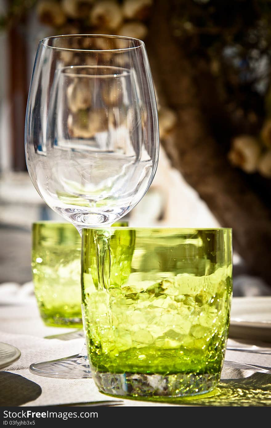 Table setting for al fresco dining in a picturesque village street with olive tree and garlic in the background, portrait. Table setting for al fresco dining in a picturesque village street with olive tree and garlic in the background, portrait.