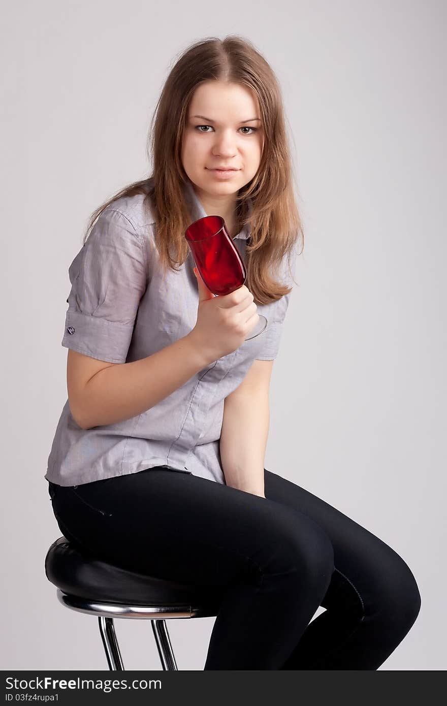 A girl in a bright red T-shirt and a glass sitting on a light background