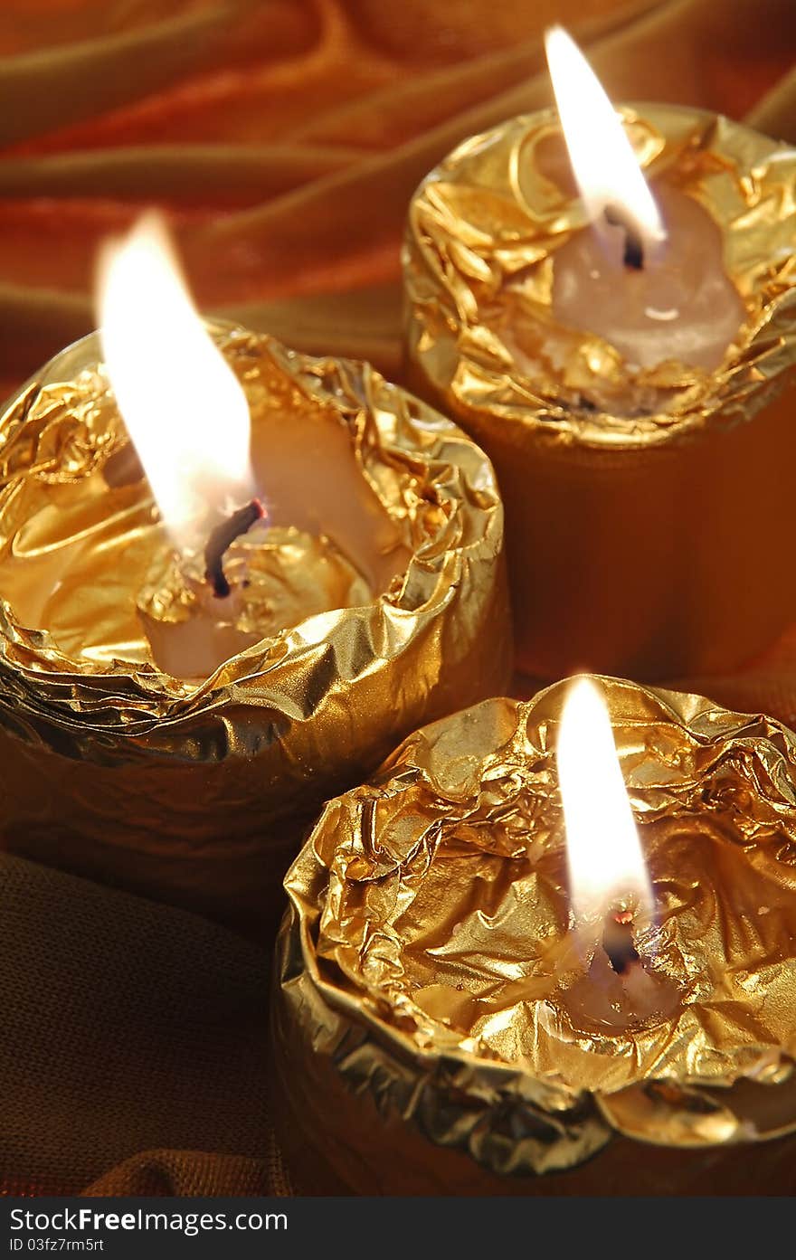 Three small burning golden candles, vertical composition