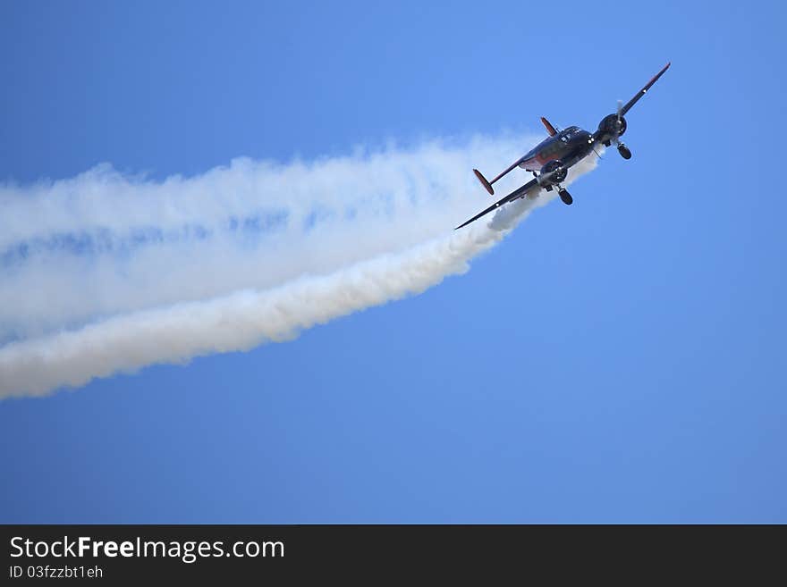 An acrobatic twin engine airplane banks hard as it streams smoke from its engines.