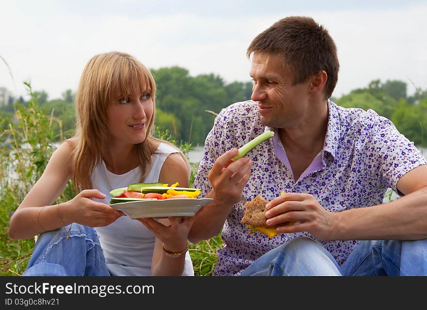 Young happy couple eating together outdoors. Young loving couple having a picnic outdoors