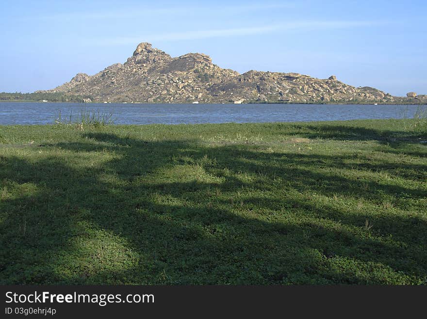 Distant rocky hill and lake with shaded lush green grassy land in foreground. Distant rocky hill and lake with shaded lush green grassy land in foreground