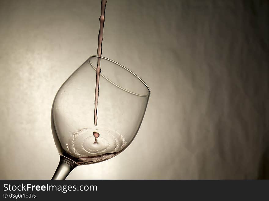 The first drop of wine being poured splashes into a wine glass. The first drop of wine being poured splashes into a wine glass