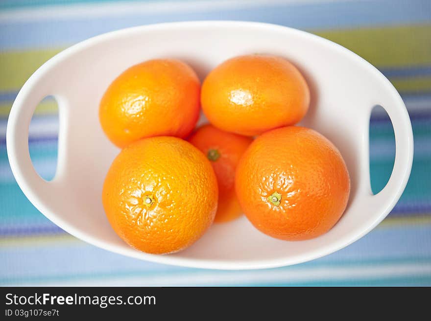 Fresh oranges in a white bowl over multicolor background.