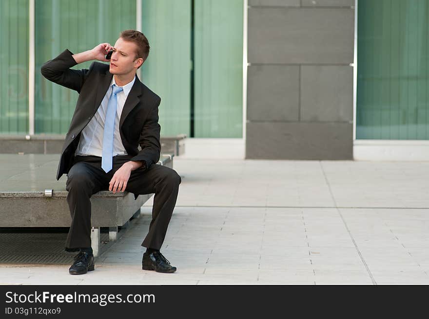 Young business man sitting with a telephone. Young business man sitting with a telephone