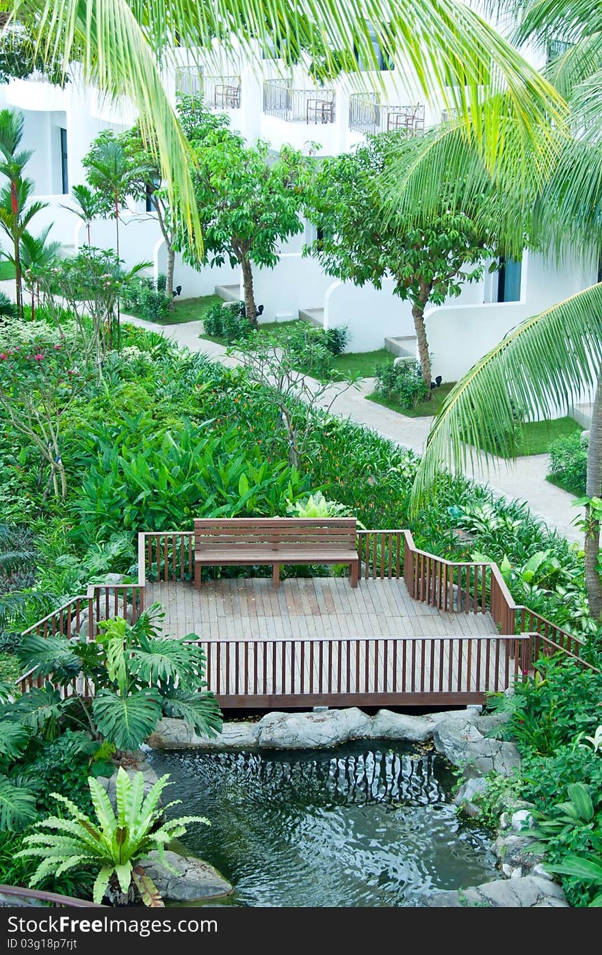 A tropical resort with wooden chair and pond surrounded by greenery