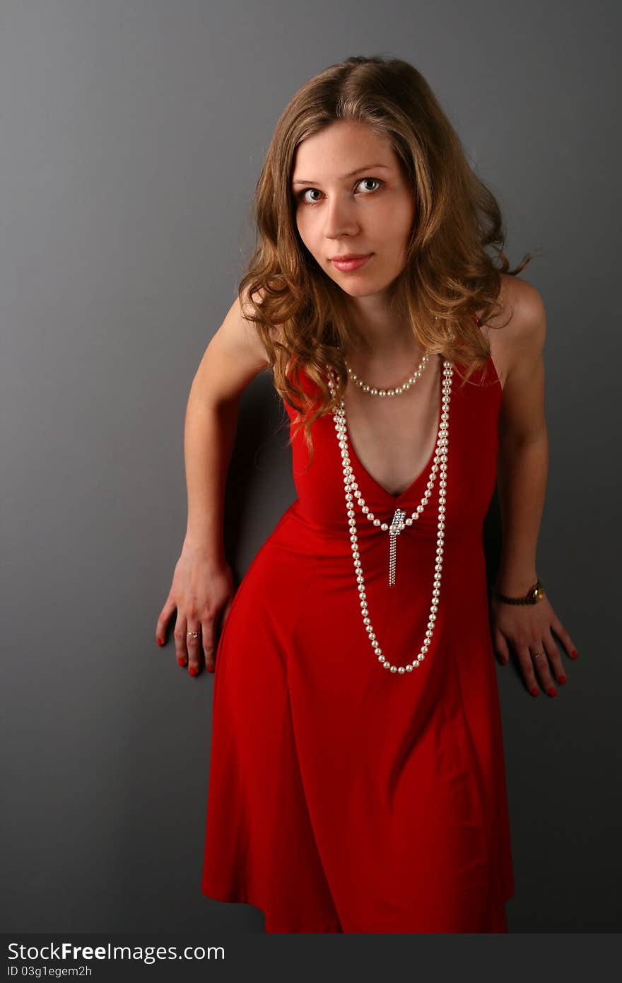 Girl in red dress posing at grey wall bending forward. Girl in red dress posing at grey wall bending forward.