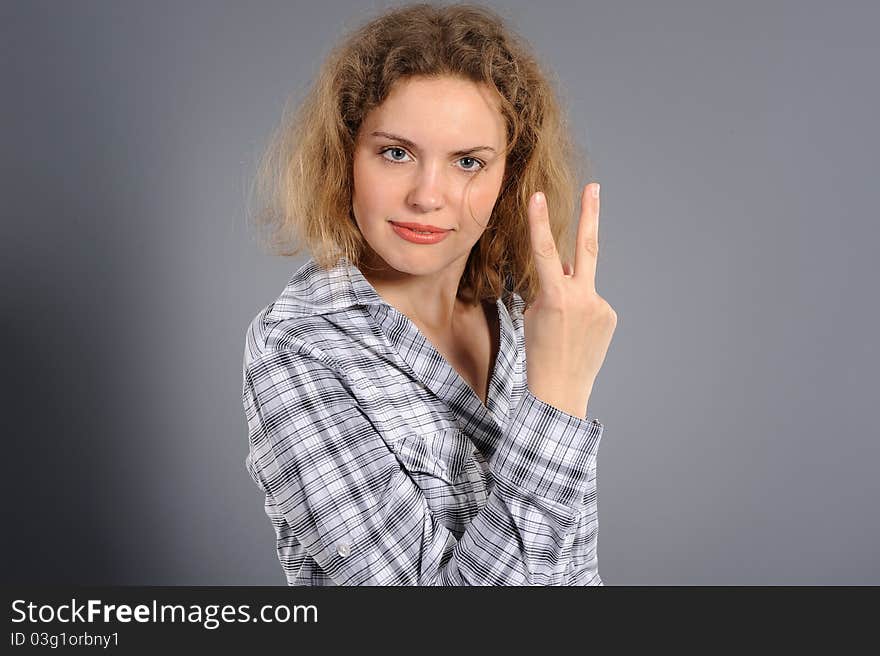 Portrait of the nice woman, showing two fingers, on a grey background