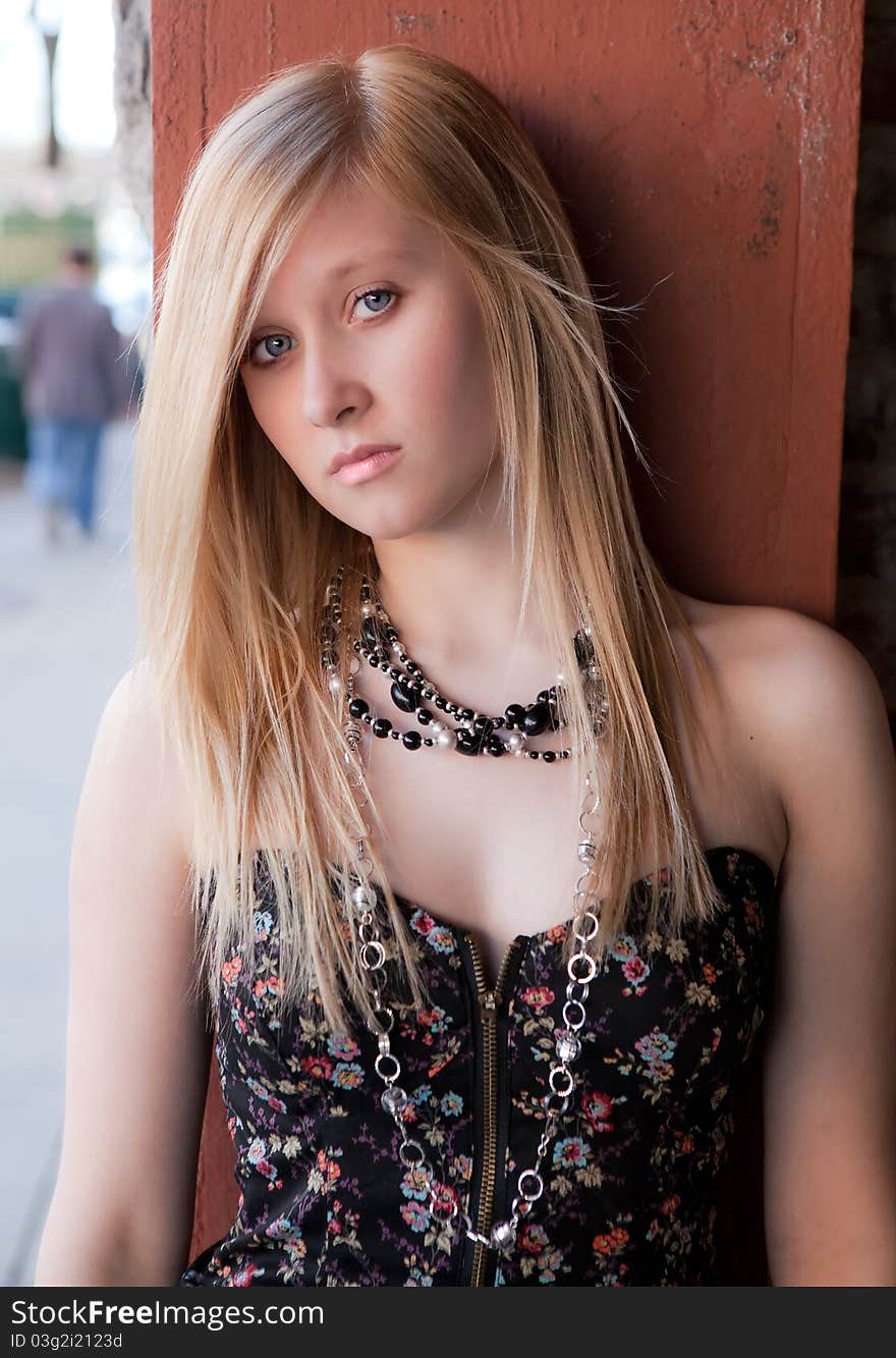 A portrait of a lovely young woman in a tube top and necklaces, posing against a wall in the downtown of a city. A portrait of a lovely young woman in a tube top and necklaces, posing against a wall in the downtown of a city