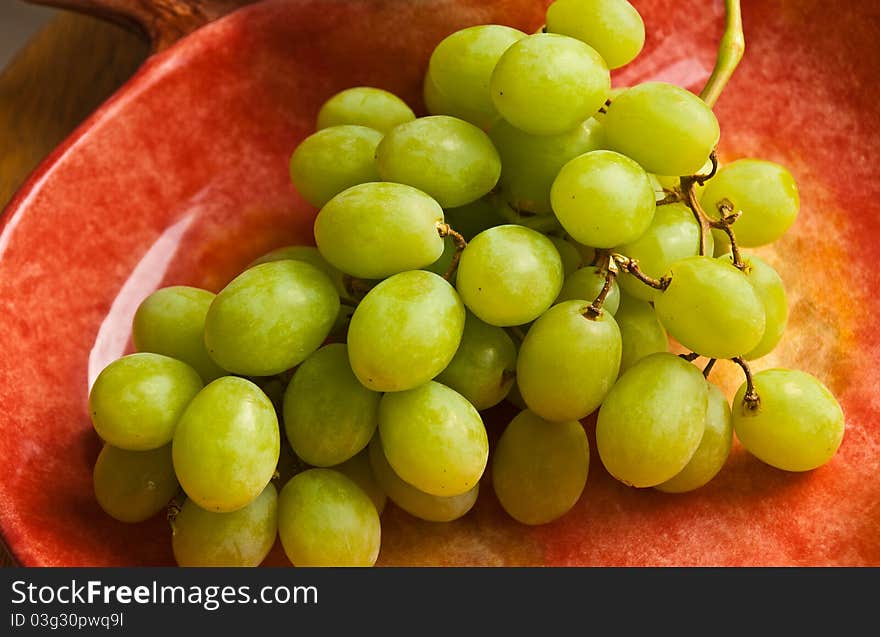 Bunch of green grapes in a light red dish. Bunch of green grapes in a light red dish