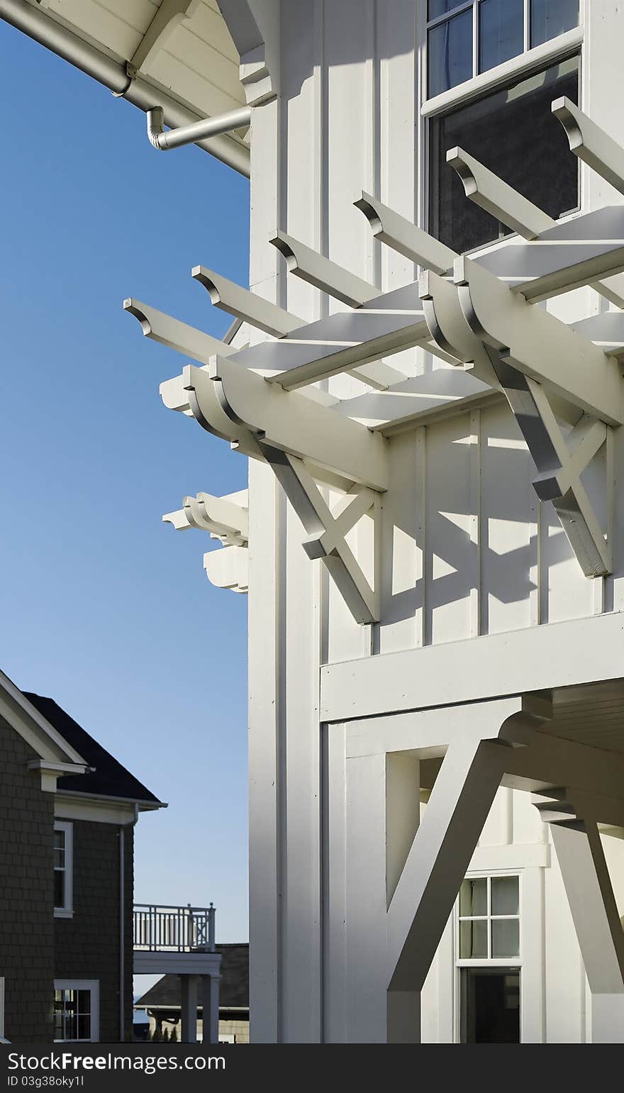 A window arbor is seen attached to a covered porch of a home. There is an open window above it. Vertical shot.