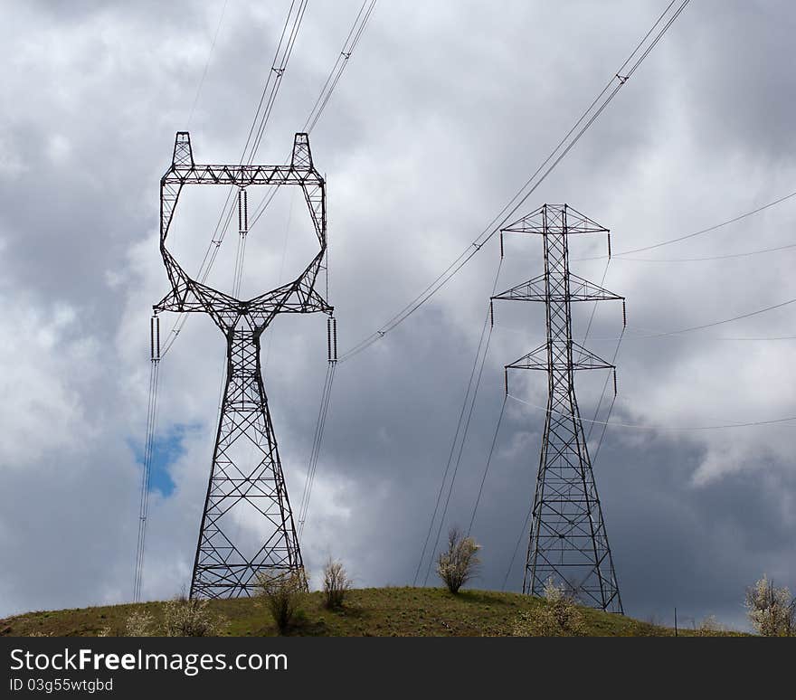 Electricity transmission towers stand on a hillside in the path of an oncoming storm. Electricity transmission towers stand on a hillside in the path of an oncoming storm.