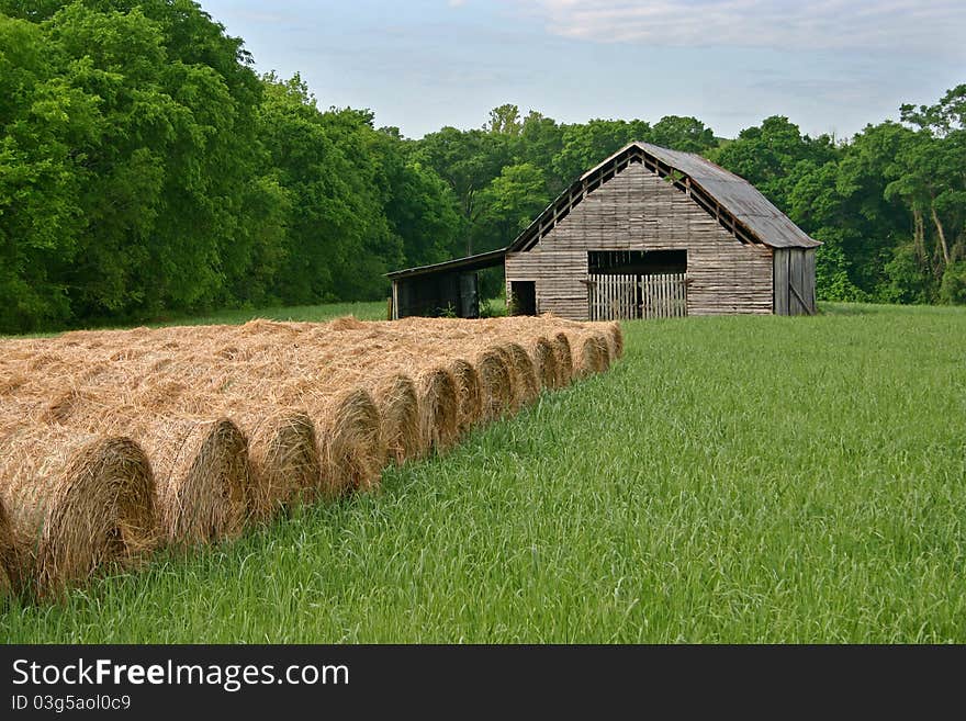 Rolls of hay in a field in front of a barn